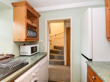 A kitchen with countertop microwave dish rack washing machine refrigerator and wooden cabinets at Beckfold Cottage in Broughton-In-Furness