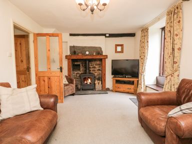A living room with leather sofas a fireplace a television and floral curtains at Beckfold Cottage in Broughton In Furness