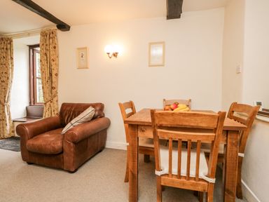 A room with a brown leather armchair a wooden dining table with four chairs and fruit on top at Beckfold Cottage in Broughton-In-Furness