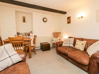 A living room with brown leather sofas wooden dining table and chairs a wall clock and a rocking chair at Beckfold Cottage in Broughton-In-Furness