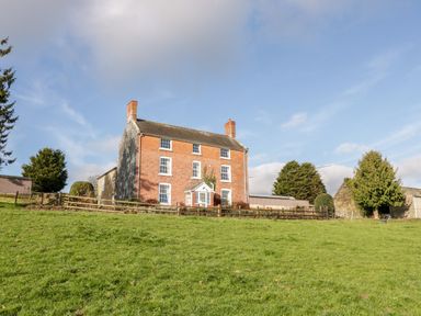A brick house with white framed windows and two chimneys on a grassy hill at Squires Rest in Llanfair Caereinion