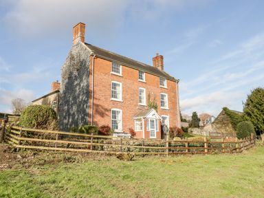 A three-story brick house with multiple chimneys and a wooden fence around the garden at Squires Rest in Llanfair Caereinion