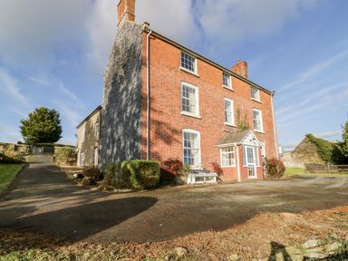 A three-story brick house with multiple windows and a small front porch surrounded by bushes and driveway at Squires Rest in Llanfair Caereinion