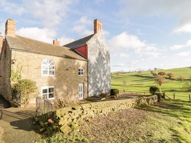 A stone house with chimneys and white windows near a stone wall and green fields at Squires Rest in Llanfair Caereinion