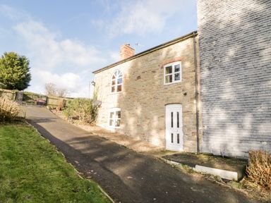 A stone cottage with white windows and door beside a paved driveway at Squires Rest in Llanfair Caereinion