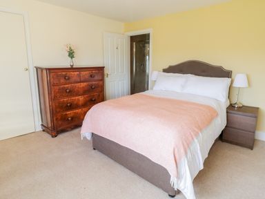 A bedroom with a bed a wooden dresser and a bedside table with a lamp at Squires Rest in Llanfair Caereinion