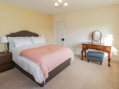 A bedroom with a double bed with white bedding and peach throw a bedside table with lamp a dressing table with mirror and blue stool at Squires Rest in Llanfair Caereinion