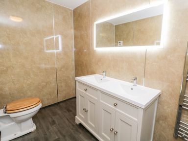 A bathroom with a double sink vanity a backlit mirror and a toilet with a wooden seat at Squires Rest in Llanfair Caereinion