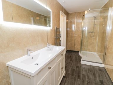 A bathroom with a double sink vanity a large mirror a heated towel rack and a curved glass shower enclosure at Squires Rest in Llanfair Caereinion