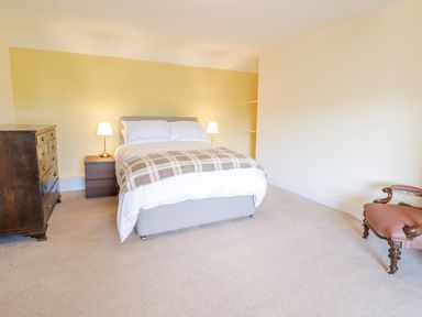 A bedroom with a bed between two bedside tables with lamps a chest of drawers and an upholstered chair at Squires Rest in Llanfair Caereinion