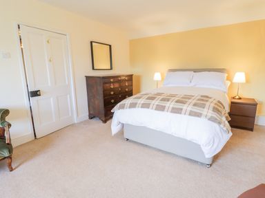 A bedroom with a bed bedside tables lamps a chest of drawers a mirror and a chair at Squires Rest in Llanfair Caereinion