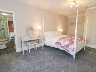 A bedroom with a four-poster bed a dressing table with a mirror two lamps carpeted floor and an open doorway to a bathroom at Squires Rest in Llanfair Caereinion