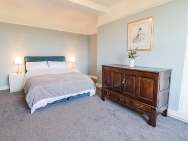 A bedroom with a bed two nightstands with lamps a wooden cabinet with flowers and a framed picture on the wall at Squires Rest in Llanfair Caereinion