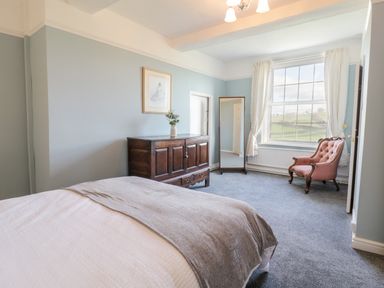 A bedroom with a bed a wooden dresser a standing mirror and a pink upholstered chair at Squires Rest in Llanfair Caereinion