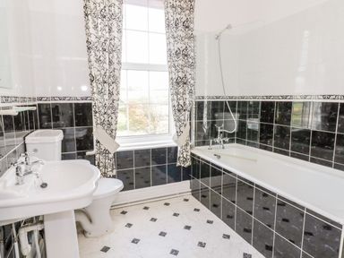 A bathroom with a bathtub shower toilet sink and a window with patterned curtains at Squires Rest in Llanfair Caereinion