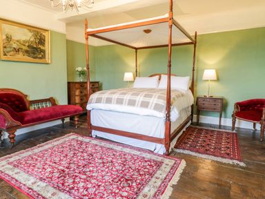 A bedroom with a four-poster bed two red chairs two rugs a chest of drawers and green walls at Squires Rest in Llanfair Caereinion