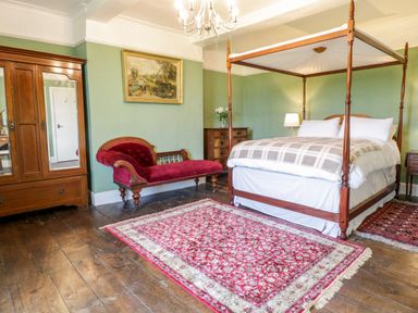 A bedroom with a wooden canopy bed red chaise lounge wooden wardrobe and red patterned rug at Squires Rest in Llanfair Caereinion