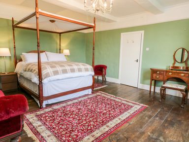 A bedroom with a four poster bed lamps a red rug wooden floor a dressing table and red chairs at Squires Rest in Llanfair Caereinion