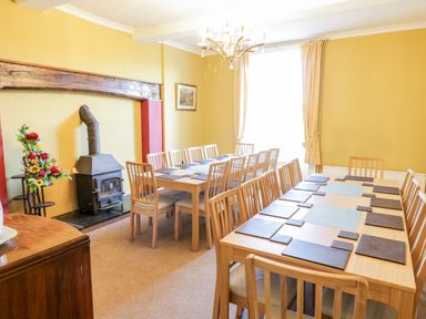 A dining room with two tables and multiple chairs near a wood stove and a window at Squires Rest in Llanfair Caereinion