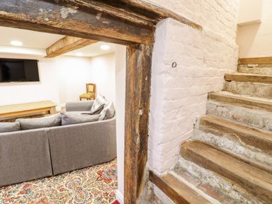 A room with a gray couch a wooden coffee table a wooden chair a mounted television and stairs with wooden steps and stone risers at Squires Rest in Llanfair Caereinion
