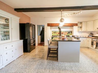 A kitchen with a black refrigerator white cabinets an island with chairs and a glass cake stand at Squires Rest in Llanfair Caereinion