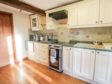 A kitchen with white cabinets a stove sink microwave toaster kettle and wooden floor at Squires Rest in Llanfair Caereinion