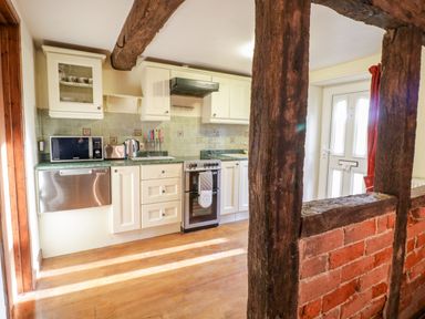 A kitchen with white cabinets a stove microwave and toaster with wood beams and a brick half wall at Squires Rest in Llanfair Caereinion