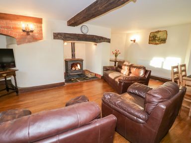 A living room with brown leather sofas a wood burning stove a television and a wooden dining table at Squires Rest in Llanfair Caereinion