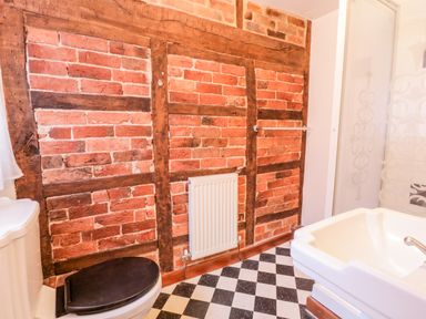 A bathroom with a toilet, sink, radiator, black and white checkered floor and exposed brick and wood wall at Squires Rest in Llanfair Caereinion