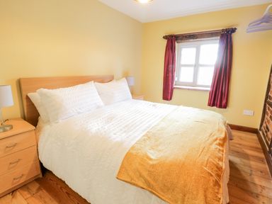 A bedroom with a double bed wooden bedside tables lamps window with red curtains at Squires Rest in Llanfair Caereinion
