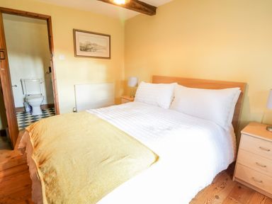 A bedroom with a double bed white bedding yellow blanket bedside tables and an en suite bathroom visible at Squires Rest in Llanfair Caereinion