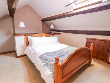 A bedroom with a wooden bed with white bedding and two lamps on a shelf under a sloped ceiling at Squires Rest in Llanfair Caereinion