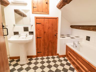 A bathroom with a pedestal sink a bathtub with wood paneling and wooden doors with exposed ceiling beams at Squires Rest in Llanfair Caereinion