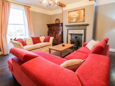 A living room with red sofas a cream sofa a wooden coffee table a fireplace and a wooden cabinet at Squires Rest in Llanfair Caereinion