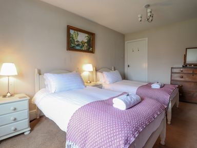 A bedroom with two single beds with pink patterned throws and white bedside tables with lamps at Squires Rest in Llanfair Caereinion