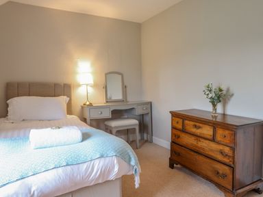 A bedroom with a bed a vanity desk with a mirror and lamp and a wooden chest of drawers with flowers at Squires Rest in Llanfair Caereinion