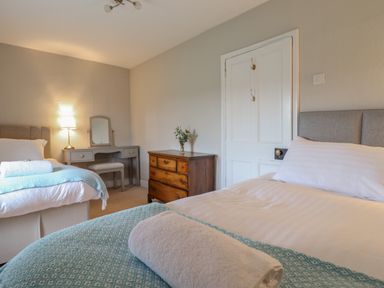 A bedroom with two beds a wooden dresser a grey vanity table with a mirror and a lamp at Squires Rest in Llanfair Caereinion