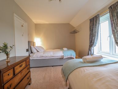 A bedroom with two single beds a wooden dresser a window with curtains and a flower vase at Squires Rest in Llanfair Caereinion