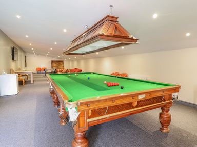 A game room with a snooker table under a large wooden light fixture with chairs and a table in the background at Squires Rest in Llanfair Caereinion
