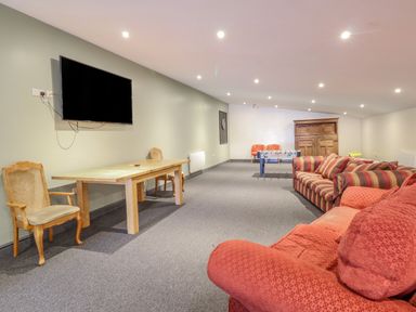 A large room with sofas a wooden table two chairs a wall-mounted television a foosball table and a wooden cabinet at Squires Rest in Llanfair Caereinion