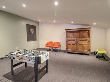 A game room with a foosball table dartboard two orange chairs wooden cabinet and toy truck at Squires Rest in Llanfair Caereinion