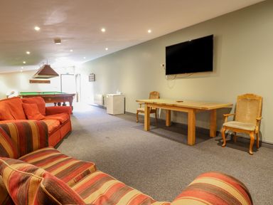 A room with a pool table red and striped sofas a wooden table two chairs a small fridge and a wall-mounted television at Squires Rest in Llanfair Caereinion