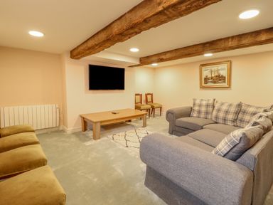 A living room with a grey sofa with plaid cushions a wall-mounted television a wooden coffee table two chairs and exposed wooden ceiling beams at Squires Rest in Llanfair Caereinion