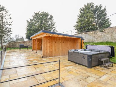 An outdoor area with a wooden shelter a hot tub and a barbecue on a stone patio at Squires Rest in Llanfair Caereinion