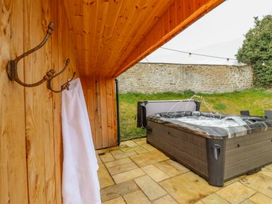 An outdoor hot tub with water jets next to a wooden wall with hooks and a white towel at Squires Rest in Llanfair Caereinion