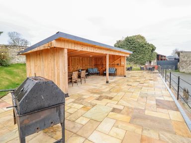 An outdoor patio area with a grill and a wooden sheltered seating area with chairs and tables at Squires Rest in Llanfair Caereinion