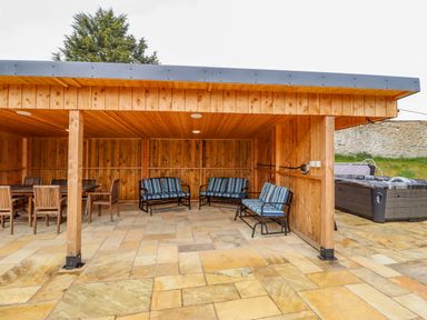 A wooden outdoor covered seating area with chairs and benches next to a hot tub at Squires Rest in Llanfair Caereinion
