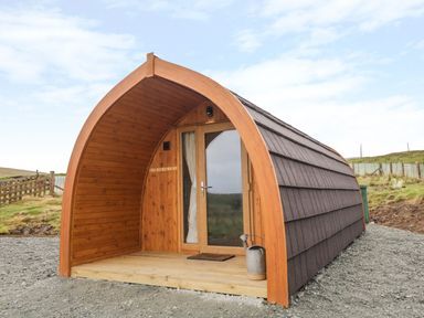 A small wooden pod with a curved roof gravel ground and a watering can outside at Garraidh Ghorm Pod in Conista