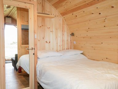 A small bedroom with a double bed white bedding and wood paneling on walls and ceiling with a mirror on the door at Garraidh Ghorm Pod in Conista