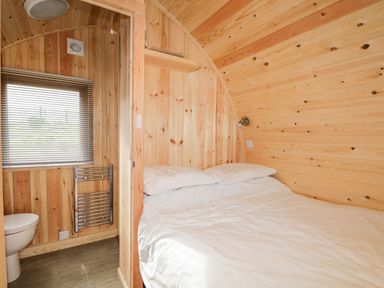 A wooden bedroom with a double bed and a small bathroom with a toilet and window at Garraidh Ghorm Pod in Conista